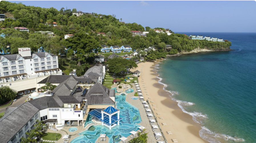 Aerial view of the Sandals resort on the St. Lucia coastline: hillside villas and a mosaic-tiled pool beside a golden beach and turquoise Caribbean water